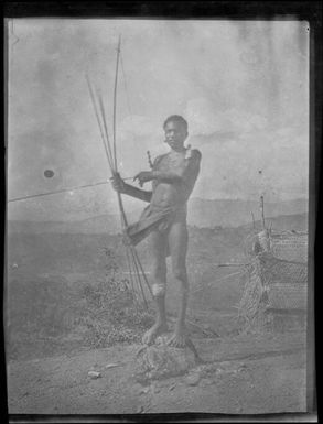 Man standing on a stone holding a bow and arrow, Papua, ca. 1923 / Sarah Chinnery