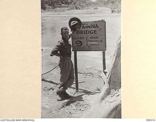 PURIATA RIVER AREA, BOUGAINVILLE. 1945-04-03. LT D. KINNA, MILITARY HISTORY SECTION, STANDING NEXT TO THE MCKINNA BRIDGE SIGNPOST. THE BRIDGE IS NAMED AFTER LT-COL J.G. MCKINNA, COMMANDING OFFICER ..