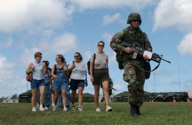 US Marine Corps (USMC) Sergeant (SGT) Terry Cree, 2nd Battalion, 11th Marine Regiment, Marine Corps Base (MCB) Camp Pendleton, California (CA), with a 5.56 mm M16A2 rilfe/M203 40 mm grenade launcher, escorts civilian and dependent evacuees to a landing zone during a simulated non-combatant evacuation operation (NEO) at US Naval Forces Marianas Support Activity, Guam. The simulated NEO is part of Exercise TANDEM THRUST 2003, a joint military endeavor including forces from the United States, Canada and Australia