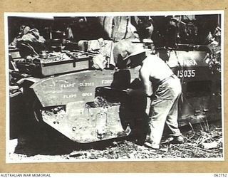 NX101785 TROOPER E. G. STEVENS OF THE 1ST TANK BATTALION GROUP WORKSHOPS, AUSTRALIAN ELECTRICAL AND MECHANICAL ENGINEERS, CLEANING MUD FROM THE CHUTES OF A MATILDA TANK