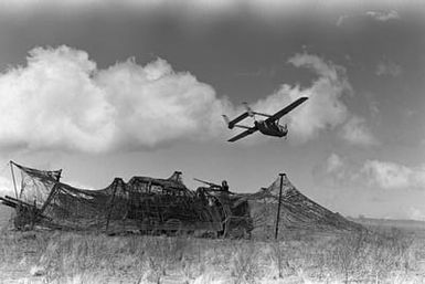 An O-2 Skymaster aircraft flies over Kilo Btry., 1ST Bn., 12th Marines, as it returns from a reconnaissance mission. The partly-camouflaged gun is a 105mm howitzer. This activity is a part of the battalion's combat readiness evaluation at the Pakalula Training Area