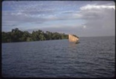 Canoe with sail up, near a small island