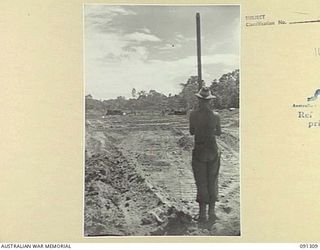 BOUGAINVILLE. 1945-04-28. A MEMBER OF 53 FIELD PARK COMPANY, ROYAL AUSTRALIAN ENGINEERS, HOLDING A STAFF DURING SIGHTING BY DUMPY LEVEL DURING THE CONSTRUCTION OF AN AIRSTRIP FOR RAAF AUSTER ..