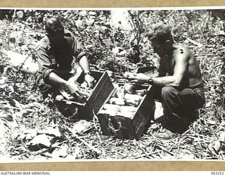 HUON GULF, NEW GUINEA. 1944-01-01. WX10831 LANCE CORPORAL G. A. CRIDDLE (1) AND WX4794 CORPORAL A. W. JAMES (2) OF THE 9TH DIVISION SALVAGE UNIT CHECKING SUPPLIES LEFT BEHIND BY THE RETREATING ..