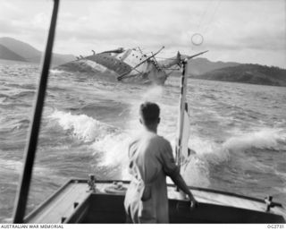 PORT MORESBY, PAPUA. C. 1944. A CREW MEMBER OF A MOTOR LAUNCH OF THE RAAF RESCUE SERVICE LOOKS AT THE WRECK OF THE MV MACDHUI WHICH WAS THE TARGET OF ATTACKS BY JAPANESE BOMBER AIRCRAFT ON ..