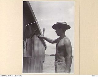 BORAM, NEW GUINEA. 1945-10-19. SERGEANT J.F. TAIT, 43 LANDING CRAFT COMPANY, PAINTING ONE OF THE FIVE BARGES WHICH WERE USED TO EVACUATE THE JAPANESE FROM THE SEPIK RIVER AREA