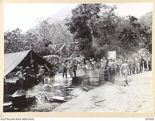 RABAUL, NEW BRITAIN. 1945-09-23. SIGNALLERS OF 11 DIVISION SIGNALS, WHO ARE HOT AND THIRSTY AND COVERED WITH DUST LINE UP AT THE COOKHOUSE FOR THEIR MORNING TEA