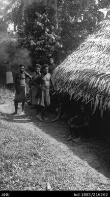 Men by grass-roof building