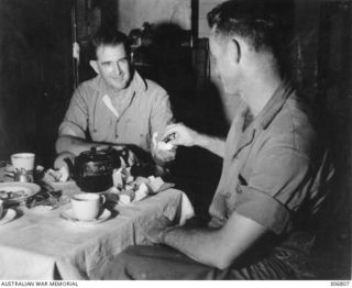 NEW GEORGIA, SOLOMON ISLANDS. 1943-03. CAPTAIN D.G. (DONALD) KENNEDY, BRITISH SOLOMON ISLANDS PROTECTORATE DEFENCE FORCE, OFFERS A ?CIGARETTE TO CAPTAIN BOYD (?COULTAS), INTELLIGENCE OFFICER, ..