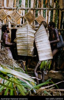 Men covered in large leaves entering a building