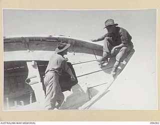 BOIKEN, NEW GUINEA. 1945-07-18. TROOPER E. GEDDES (1) AND TROOPER D.D. SMITH (2), MEMBERS OF 2/2 FIELD REGIMENT, ROYAL AUSTRALIAN ARTILLERY, EXAMINING A LIFEBOAT WHICH WAS BURIED BY THE JAPANESE ..