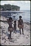 Girls on a beach near Kaibola village, wearing short fiber skirts, woman in background gathers shellfish