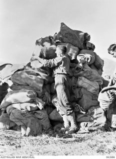 DUMPU, NEW GUINEA. 1943-12-22. NX41886 PRIVATE A. K. ORR OF FORWARD POST OFFICE 28, 7TH AUSTRALIAN DIVISION POSTAL UNIT, STACKING BAGS OF CHRISTMAS LETTERS AND PARCELS