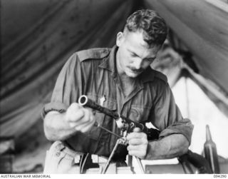 KARAWOP, NEW GUINEA. 1945-07-19. STAFF SERGEANT W.J. TOPE, CORPS OF AUSTRALIAN ELECTRICAL AND MECHANICAL ENGINEERS, ATTACHED 2/6 CAVALRY (COMMANDO) REGIMENT, ADJUSTING A BREN GUN IN THE ARMOURER'S ..