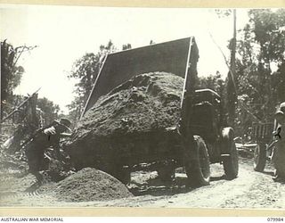 TOKO-BARARA ROAD, BOUGAINVILLE, SOLOMON ISLANDS. 1945-03-28. TIP- TRUCKS FROM THE 15TH FIELD COMPANY, ROYAL AUSTRALIAN ENGINEERS, UNLOAD TOP DRESSING TO COVER CORDUROY ON THE ROAD SURFACE FORMED BY ..