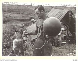 WEWAK AREA, NEW GUINEA. 1945-06-05. WARRANT OFFICER C.J. PADDICK, 3 MOBILE METEOROLOGICAL FLIGHT, RAAF, ATTACHED HEADQUARTERS ROYAL AUSTRALIAN ARTILLERY 6 DIVISION, FILLING A BALLOON FROM A ..