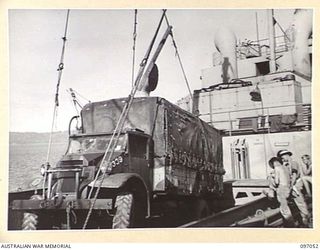 RABAUL, NEW BRITAIN. 1945-09-20. TROOPS OF 28 INFANTRY BATTALION STAND BY AS A VEHICLE IS BEING LIFTED FROM THE HOLD OF THE ANDREW BRISCOE, THE FIRST VICTORY SHIP TO REACH RABAUL WITH SUPPLIES