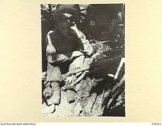 BOUGAINVILLE ISLAND, 1945-01-21. QX53505 LIEUTENANT M. ANDERSON, 42ND INFANTRY BATTALION CONTACTING THE BATTALION HEADQUARTERS FROM HIS WATER-LOGGED DUGOUT AFTER AN ALL NIGHT VIGIL AGAINST POSSIBLE ..