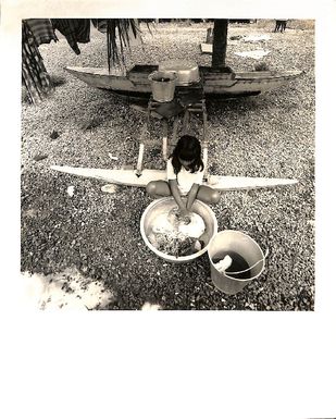 Photo of a young girl sitting on end of canoe, hand-washing clothes out of a basin.