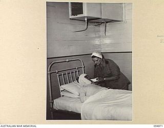LAE AREA, NEW GUINEA. 1945-08-11. PRIVATE W. HENRY (1), BEING FED BY SISTER M.B.M. BULGIN (2), IN AN AIR CONDITIONED WARD, DURING TREATMENT AT 2/7 GENERAL HOSPITAL