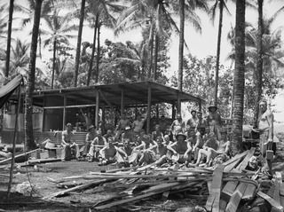 Personnel of the 33rd Docks Operating Company eating lunch near their newly erected kitchen in the Palmalmal plantation.
1. VX80375 Sapper (Spr) Ernest Edward Evans; 2. 22176 (NX113817) Corporal ..