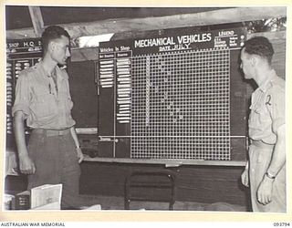 PALMALMAL PLANTATION, JACQUINOT BAY, NEW BRITAIN, 1945-06-06. CAPTAIN H.W. BARKER (1) AND SERGEANT S. AARONS (2) AT THE VEHICLE PROGRESS BOARD, 1 INFANTRY TROOPS WORKSHOP. IT SHOWS THE DAILY ..