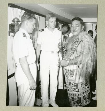 The picture depicts two crewmen in white uniforms standing together with a man in local clothes. The picture is from a reception on board in Älvsnabens gunrum for local dignitaries in Pago-Pago, Samoa. In the middle, the ship’s 2 is visible. Vessel Instant (FP2), Peder Ribbing.