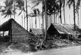 Men by thatched-roof sleeping quarters, New Caledonia, 1940s