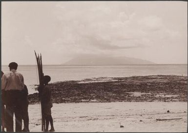 Man and two boys on beach at Rowa with Ureparapara in background, Banks Islands, 1906 / J.W. Beattie