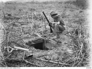 YAMIL AREA, NEW GUINEA, 1945-07-06. PRIVATE H. DAVIDSON, D COMPANY, 2/5 INFANTRY BATTALION, INSPECTING ONE OF THE 120 JAPANESE WEAPON PITS ON KUNAI RIDGE. JAPANESE EQUIPMENT AND UNEXPLODED ..