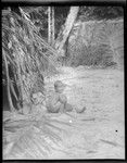 Small boy, crouching beside dwelling