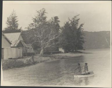 Two people in a boat with a European style building in the background, Samarai, Papua, ca. 1929 / Sarah Chinnery