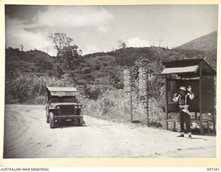 RABAUL, NEW BRITAIN. 1945-09-29. CORPORAL TIDYMAN, 11 DIVISION PROVOST COMPANY, DIRECTING TRAFFIC AT THREE WAYS, MALAGUNA ROAD. THE UNIT SIGNPOSTS POINT TOWARDS THE TUNNEL HILL ROAD