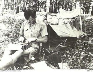 KOKODA, NEW GUINEA. 1942-10. INFORMAL PORTRAIT OF TOM FAIRHALL, SYDNEY DAILY TELEGRAPH, TAKEN IN A RUBBER PLANTATION AT KOKODA DURING THE BUNA CAMPAIGN. HE IS TYPING ON HIS TYPEWRITER