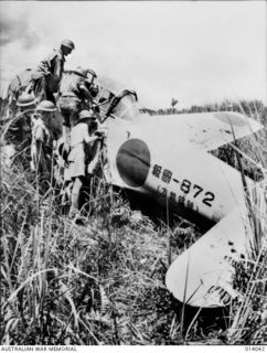 1943-01-08. PAPUA. BUNA. CAPTURED AIR STRIP AT BUNA. JAPS LEFT BEHIND PLANES STRAFED BY ALLIED FIGHTERS. NOTE BULLET HOLES IN WING OF ZERO. THIS IS ONE OF THE NEW TYPE SQUARE WING ZERO AIRCRAFT