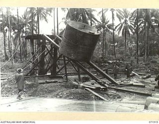 MILNE BAY, PAPUA, NEW GUINEA. 1944-03-31. MEMBERS OF THE 1ST FIELD SQUADRON, ROYAL AUSTRALIAN ENGINEERS, SLIDE A 6,000 GALLON DIESEL OIL TANK INTO POSITION ON A STAND, USING A POWER DRIVEN WINCH ..