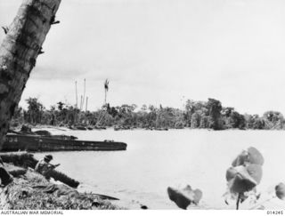 1943-01-27. PAPUA. SANANANDA AREA. ON SANANANDA BEACH AN AUSTRALIANS READY TO FIRE AT THE FIRST SIGN OF ANY JAPANESE IN THE DERELICT BARGE. IN THE BACKGROUND ARE FURTHER JAPANESE LANDING BARGES. ..