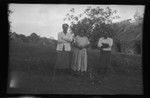 Three Fijian people in front of a traditional house