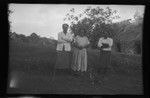 Three Fijian people in front of a traditional house