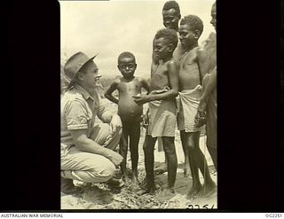 TOROKINA, BOUGAINVILLE ISLAND, SOLOMON ISLANDS. C. 1945-02. 37747 CORPORAL R. G. KAHLER, MACKAY, QLD, MAKES FRIENDS WITH A GROUP OF CHILDREN AT A NATIVE VILLAGE AT TOROKINA