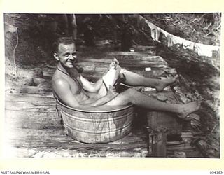 YAMIL 2, NEW GUINEA. 1945-07-20. PRIVATE D.R. HARTMANN-HUDSON, IN CHARGE OF LAUNDRY AT THE MAIN DRESSING STATION, 2/2 FIELD AMBULANCE WITH WORK FINISHED FOR THE DAY RECLINES IN A TUB OF HOT WATER ..