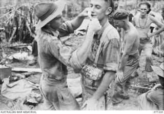 VX11580 Lieutenant J Deacon, second from left (1) having his jaw wound dressed by Q16901 Private C Manley, left (2) at the unit Rgimental Aid Post during an attack on enemy positions on Little ..