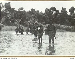 AYR, NEW GUINEA, 1943-10-21. AUSTRALIAN AND NEW GUINEA ADMINISTRATION UNIT NATIVE CARRIERS CROSSING A SHALLOW RIVER BETWEEN WIDERU AND AYR