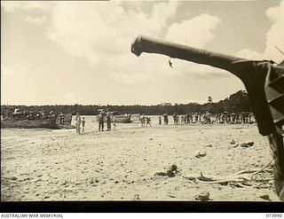 DUGUMUR BAY, NEW GUINEA. 1944-06-14. STORES FOR 4TH INFANTRY BATTALION BEING UNLOADED FROM BARGES. AN ANTI-TANK GUN STANDS IN THE FOREGROUND