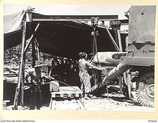 BOUGAINVILLE. 1945-08-30. TROOPS OF 113 BRIGADE WORKSHOP CORPS OF AUSTRALIAN ELECTRICAL AND MECHANICAL ENGINEERS UNLOADING LOGS FROM A RECOVERY VEHICLE AT THE WORKSHOP. LOCAL TIMBER IS USED IN THE ..