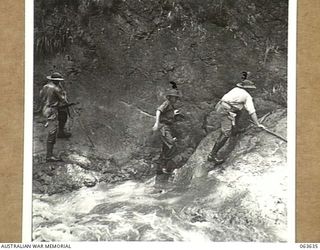 FARIA RIVER, RAMU VALLEY, NEW GUINEA. 1944-01-18. MEMBERS OF THE 2/10TH INFANTRY BATTALION CLAMBERING ALONG THE ROCK FACED BANK OF THE FARIA ON THE WAY TO GUY'S POST. THEY ARE: QX37690 SERGEANT R. ..