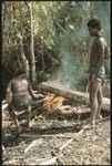 Two men heating log to remove bark