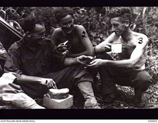 DUMPU, NEW GUINEA. 1943-10-15. AN NCO OF THE 2/27TH AUSTRALIAN INFANTRY BATTALION SHARES HIS CAKE FROM HOME AFTER THE TREVOR'S RIDGE ACTION. LEFT TO RIGHT: SX12508 CORPORAL P. J. CAREY; SX17753 ..