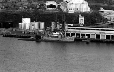 Aerial port view of the nuclear-powered attack submarine USS INDIANAPOLIS (SSN-697) and the salvage ship USS CONSERVER (ARS-39) moored abreast. The ships are in port to provide assistance after hurricane Iwa passed through the area