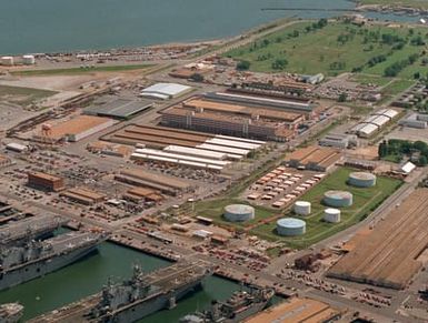 An aerial view of a section of the base showing piers 5 through 9. Tied up on the north side of pier 7 is the amphibious assault ship USS WASP (LHD-1) with the USS SAIPAN (LHA-2) on the south side of the pier. The USS NASSAU (LHA-4) is tied up on the south side of pier 6. Various other warships and auxiliaries are also moored at the different piers